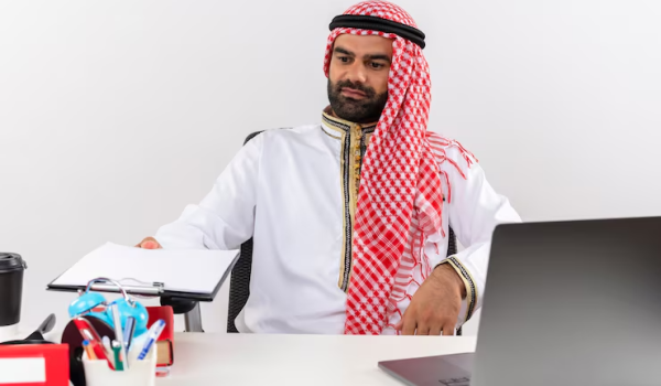 arabic-businessman-traditional-wear-sitting-table-with-laptop-computer-holding-clipboard-with-blank-